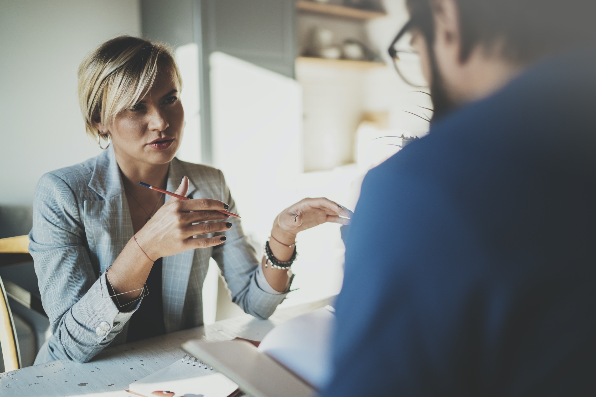 Coworkers working process at home.Young blonde woman working together with bearded colleague man at modern home office.People making conversation together.Blurred background.Horizontal.